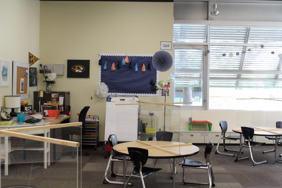 These classrooms in the Lower School often have bookshelves and other furniture, but in order to make room for distanced desks the furniture has been moved out and plexiglass has been put on the desks.