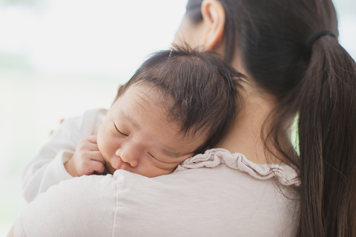 A new mother is holding her sleepy newborn son on her shoulder. The baby is fast asleep.